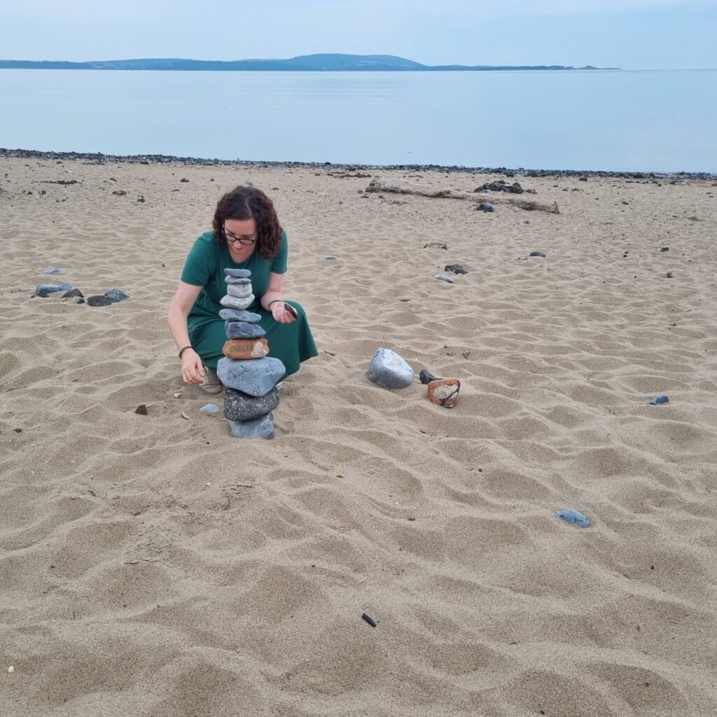 Sophie (founder of calm-nest organising) stacking stones on a beach